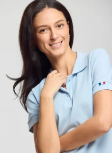 Personne souriante portant un polo bleu ciel de fabrication textile française avec un détail tricolore sur la manche.