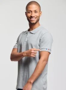 Personne souriante portant un polo gris de fabrication textile française et montrant un détail tricolore sur la manche.