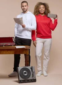 Deux personnes portent des sweats à capuche, l'un blanc et l'autre rouge, illustrant une collection de fabrication textile française.