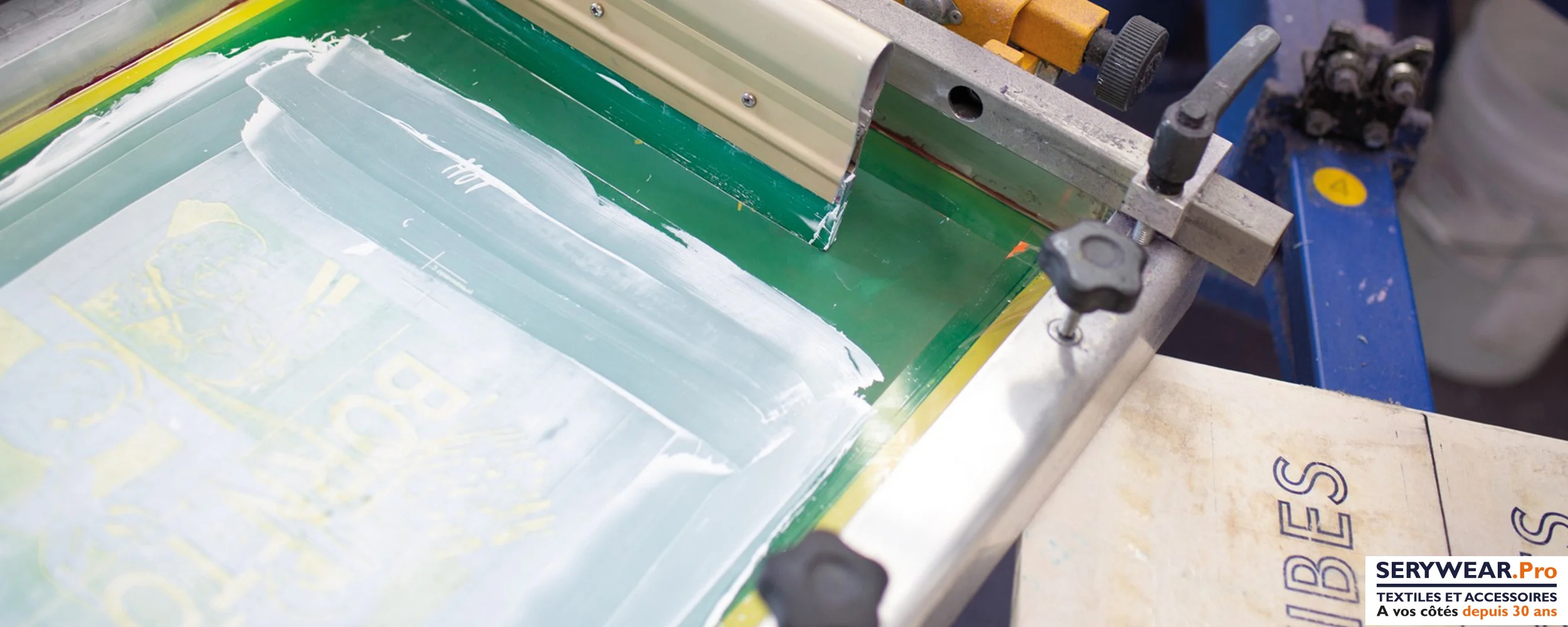 Écran de sérigraphie avec encre blanche et racle, prêt pour l'impression de textiles personnalisés dans l'atelier SERYWEAR.Pro.
