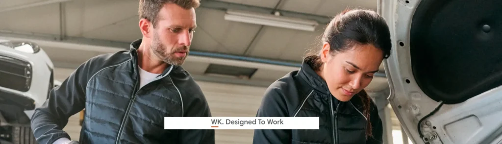 Deux professionnels portant des vestes de travail WK. Designed To Work interviennent sur un véhicule dans un atelier automobile.